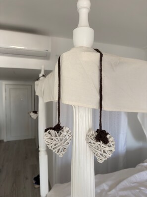 A white bed with a white canopy, two heart-shaped decorations hanging from the canopy, and a white door in the background.
