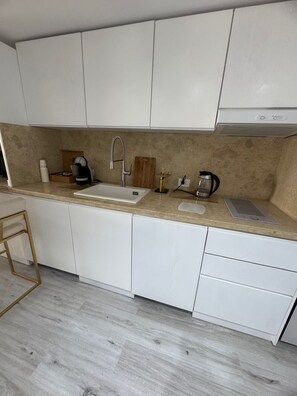 A modern kitchen with white cabinets, a stainless steel sink, and a countertop with a coffee maker, toaster, and other appliances.