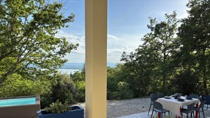 Zona pranzo all'aperto con vista sul mare, una piscina e piante in vaso.