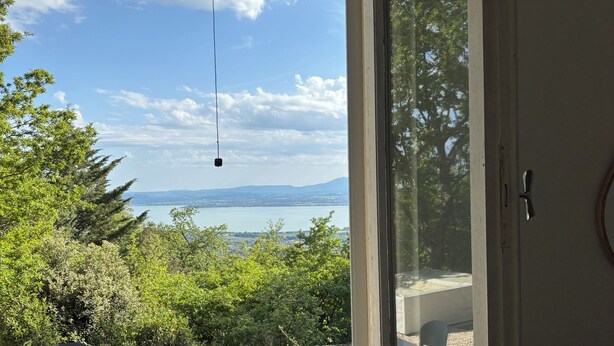 Una stanza con un'ampia finestra che si affaccia su un paesaggio con alberi e colline lontane.