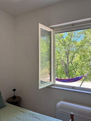 Una camera da letto con finestra, un letto, un comodino con una lampada e un termosifone.
