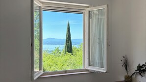 Una stanza con una finestra vista paesaggio, un termosifone, una sedia di legno e un tavolino con un vaso.