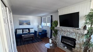 A living room with a stone fireplace, a flat-screen TV, and a blue sofa.