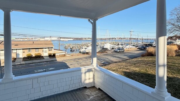 A covered porch with a view of a marina and buildings in the background.