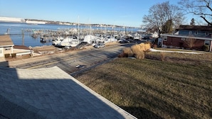 A marina with boats docked, a clear sky, and a residential area with houses and a grassy field.