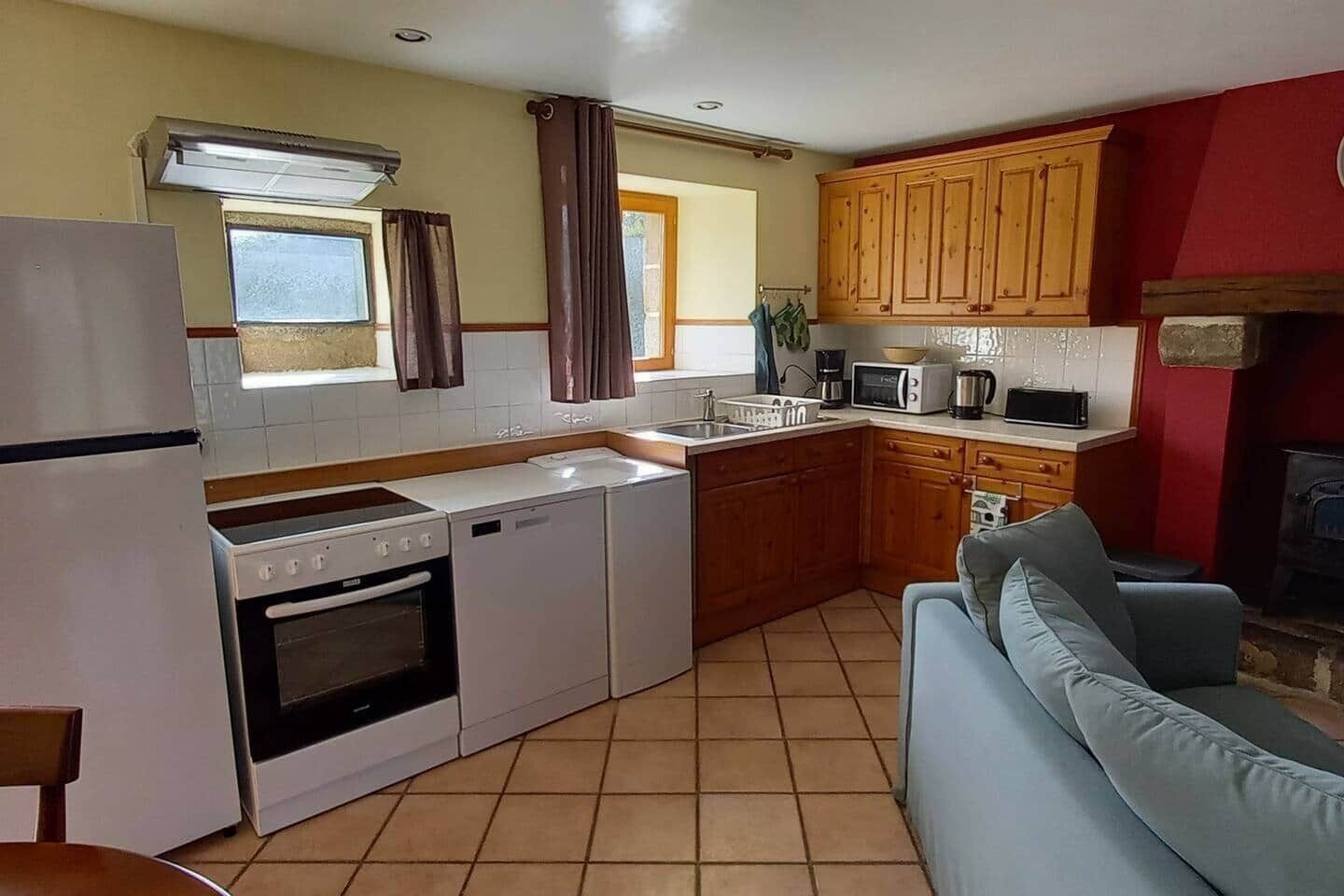Una cucina funzionale con piano cottura, forno, microonde e lavello. Nell'area soggiorno, un armadietto in legno e un divano blu.