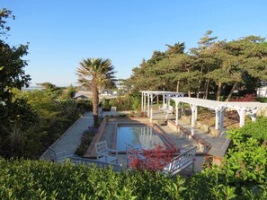 Un área de piscina con una pérgola, rodeada de exuberante vegetación y árboles.