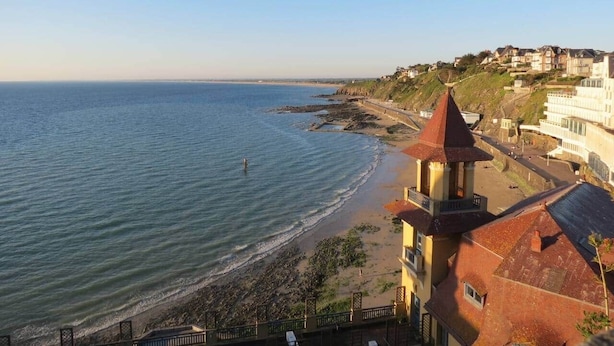 A coastal view with a building featuring a tower, a beach, and a distant shoreline.