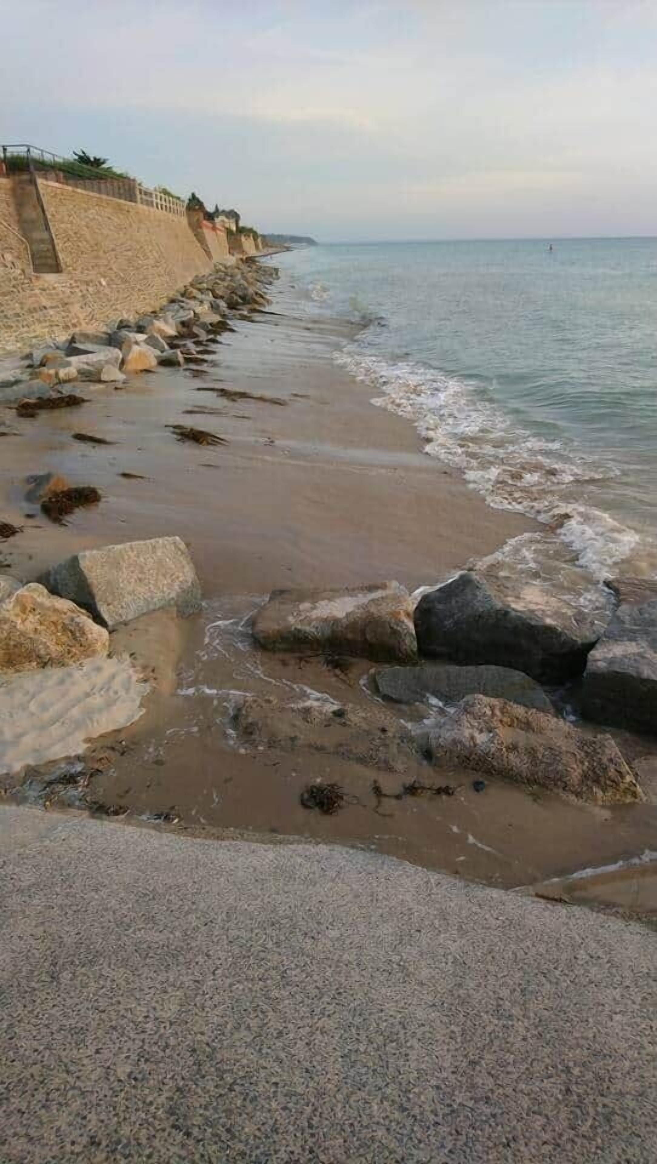 Une plage côtière bordée d’un mur de pierres et de gros rochers.