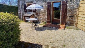 A stone building with a gravel patio, a table with chairs, and a large umbrella.