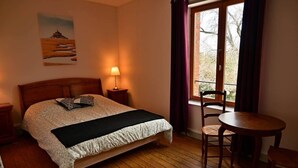 Een slaapkamer met een bed, een bedlampje, een raam met gordijnen, een stoel en een kleine tafel.