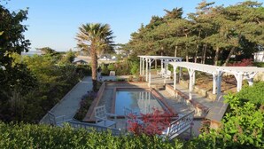 Een zwembadgedeelte met een pergola, omringd door weelderige begroeiing en bomen.