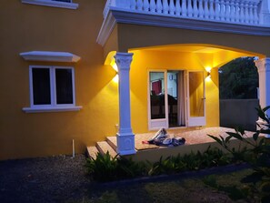 A yellow building with a covered patio, white columns, and a sliding glass door. - Rented apartment for 4 people, about 15 minutes from the beach. (Cap malheureux)