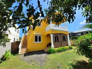 A yellow house with a white balcony, a window, and a door with a checkered pattern. - Rented apartment for 4 people, about 15 minutes from the beach. (Cap malheureux)