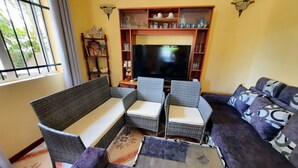 Ein Wohnzimmer mit einer Couch, zwei Sesseln, einem Fernseher und einem Regal mit Dekoration.