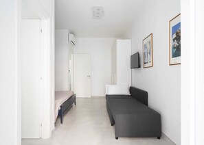 Una habitación pequeña y moderna con una cama, un sofá, un televisor y cuadros enmarcados en la pared.