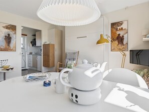 Een moderne woonkamer met een ronde tafel, witte meubels, een gele vloerlamp en kunstwerken aan de wanden.
