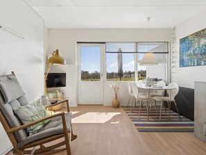 Een moderne woonkamer met een bank, een eettafel met stoelen, een televisie en een groot raam met uitzicht.