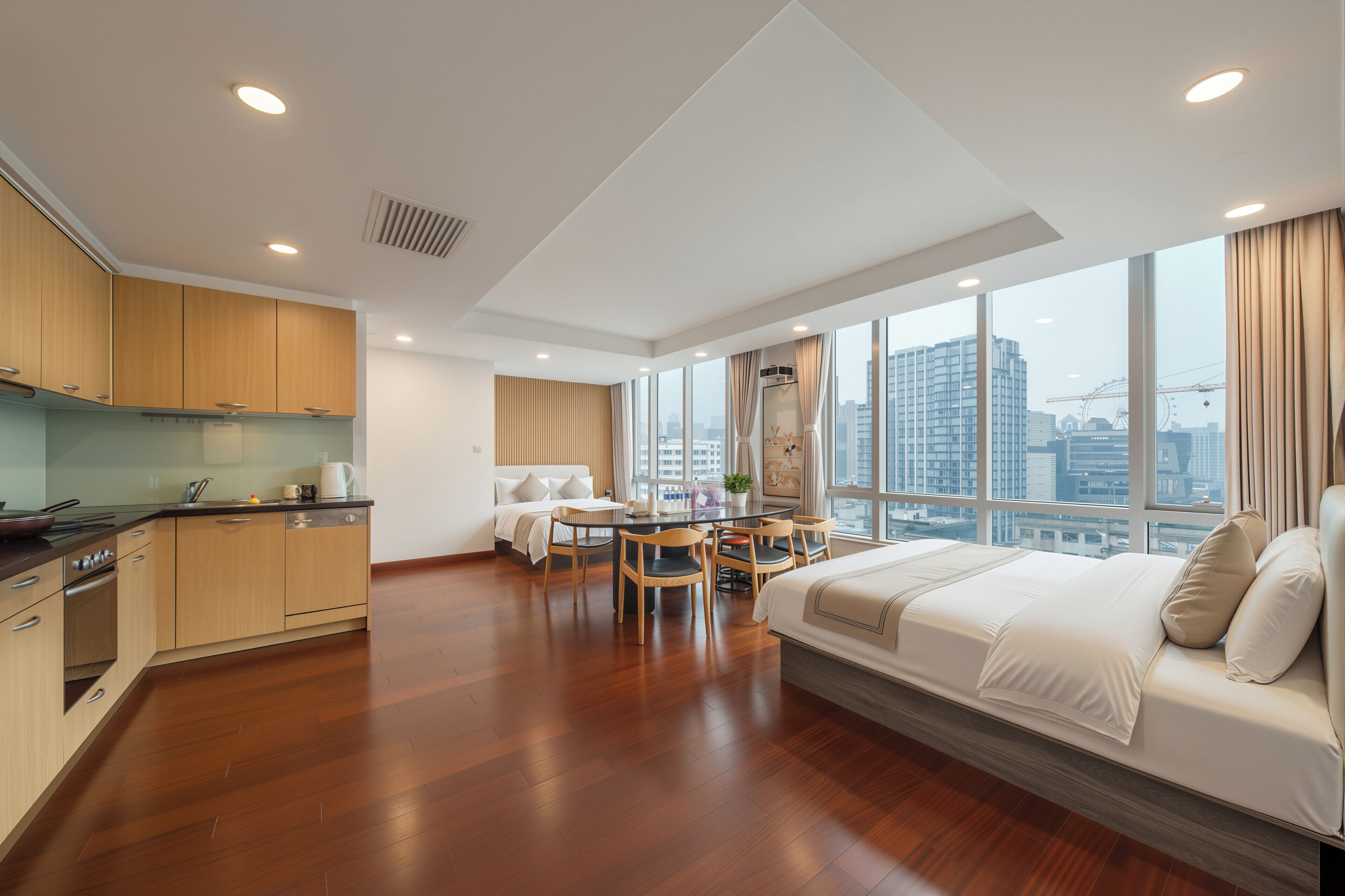 A modern hotel room with a kitchen, dining area, and a large bed.