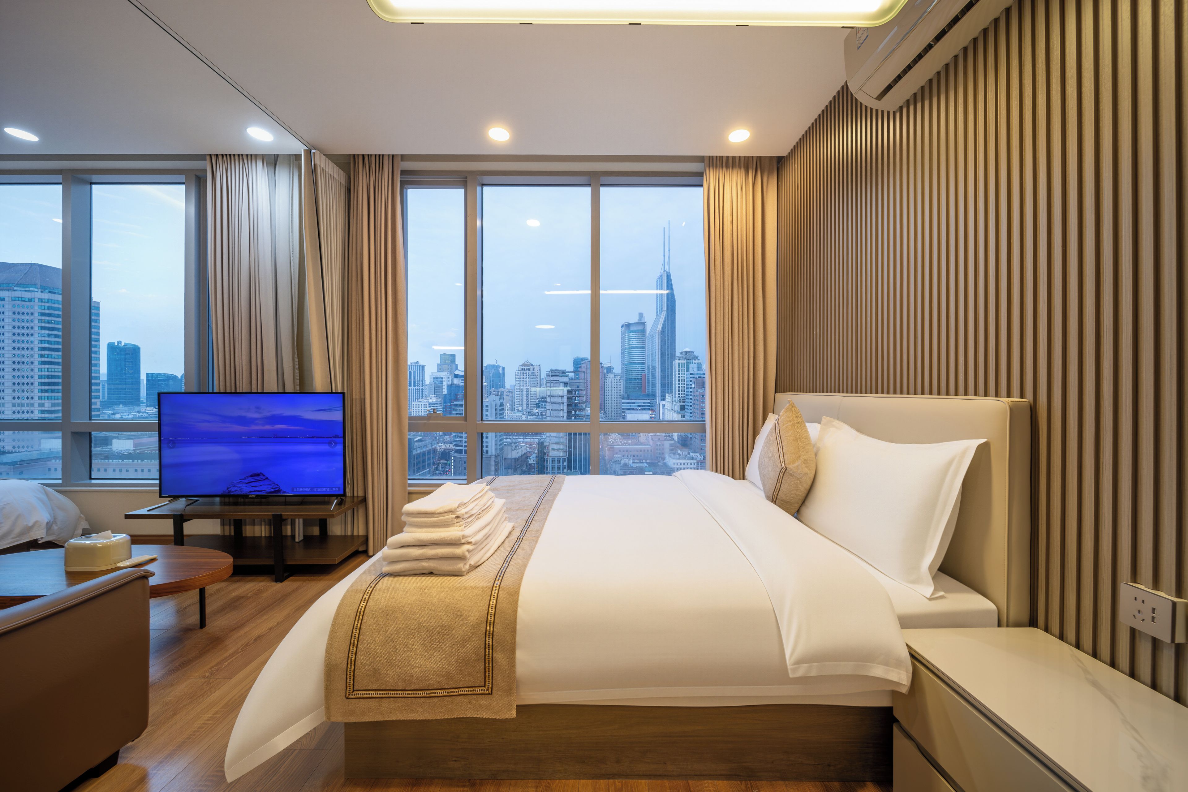 A hotel room with a bed, a TV, and a city view.