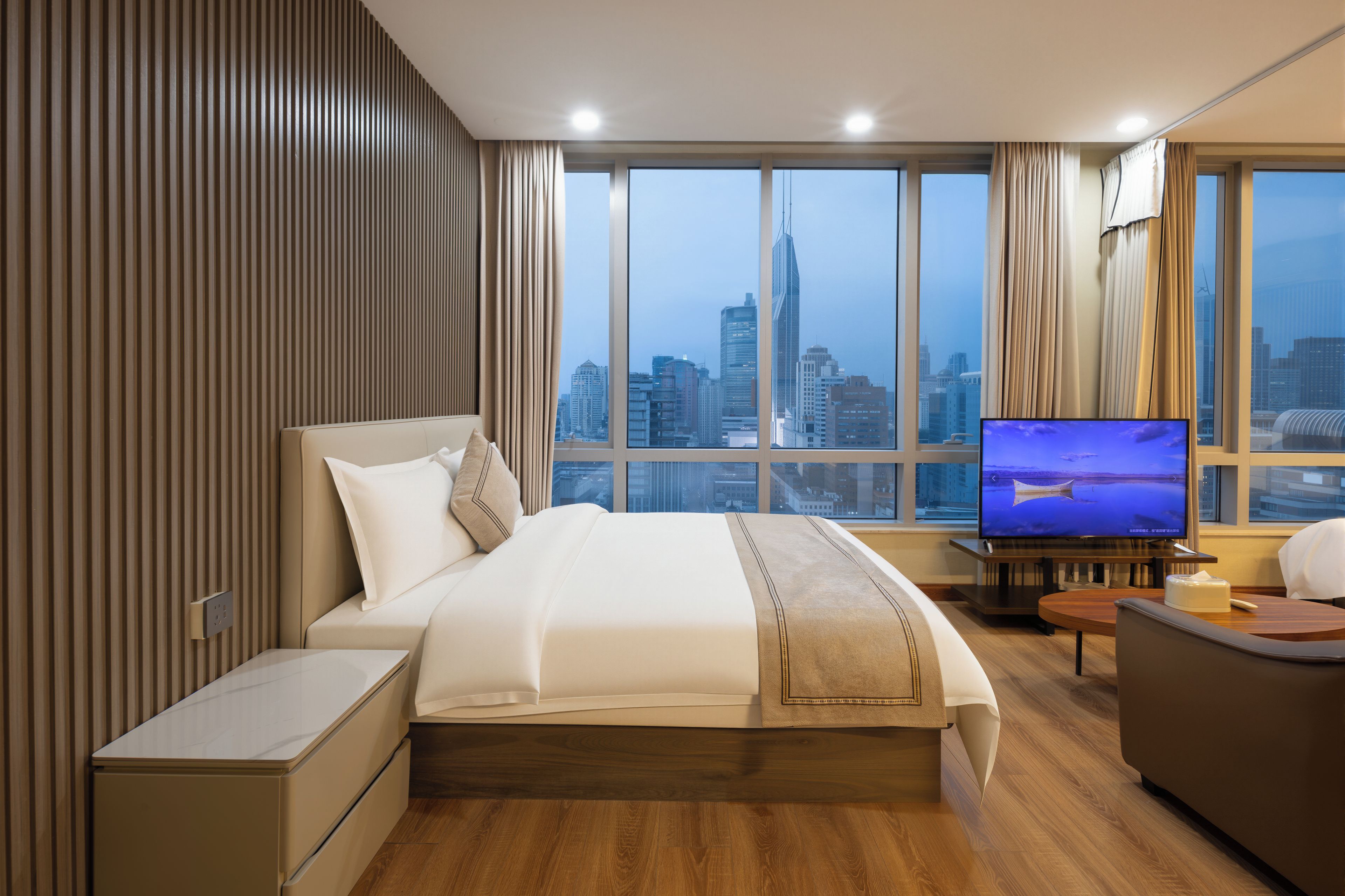 A modern hotel room with a large bed, a TV, and a view of a city skyline.
