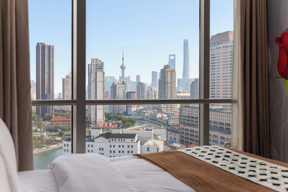 Une chambre d’hôtel dotée d’une grande fenêtre donnant sur le paysage urbain, avec une vue imprenable sur une tour imposante et une rivière.