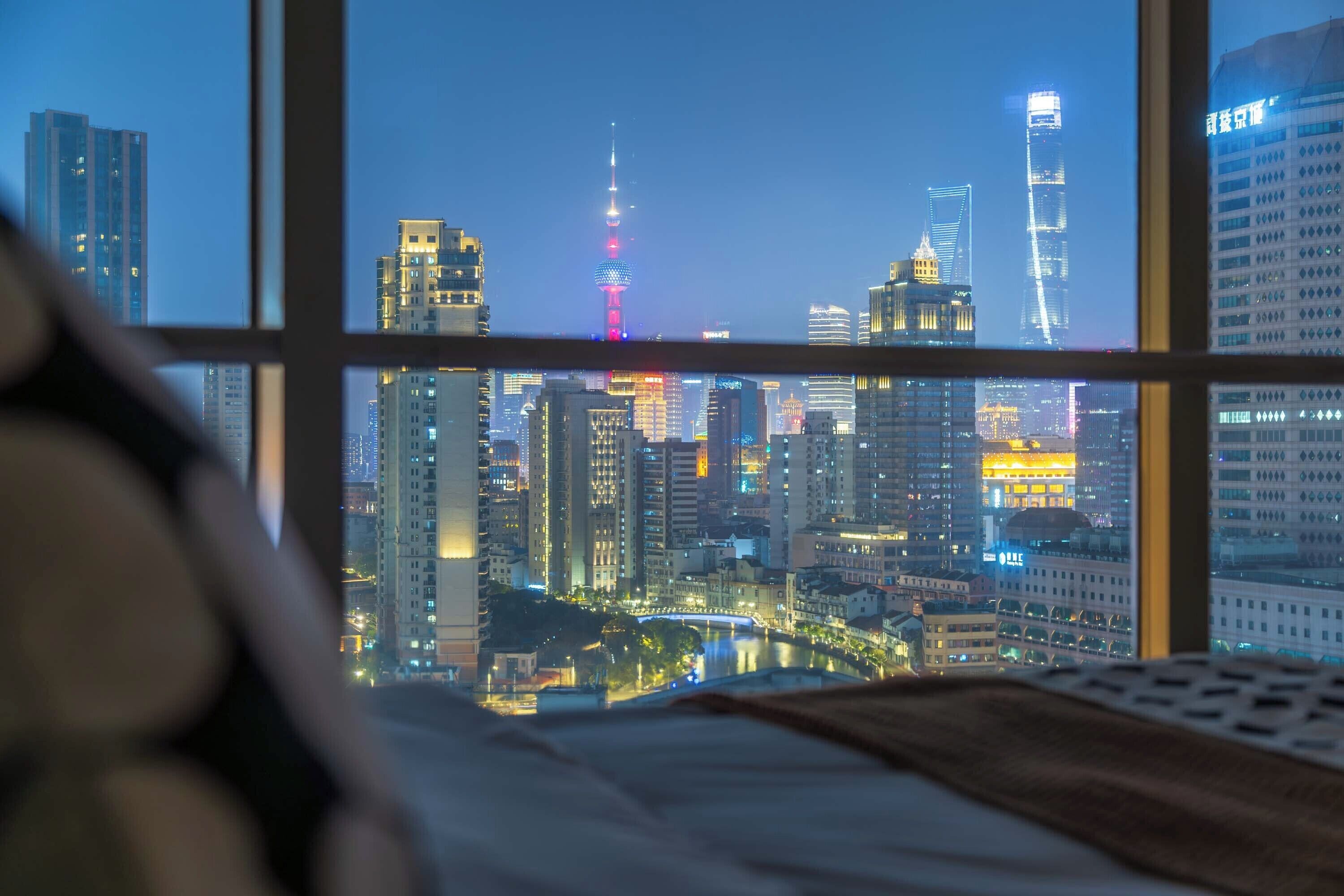 A cityscape view from a window, featuring high-rise buildings and a prominent tower with red lighting.
