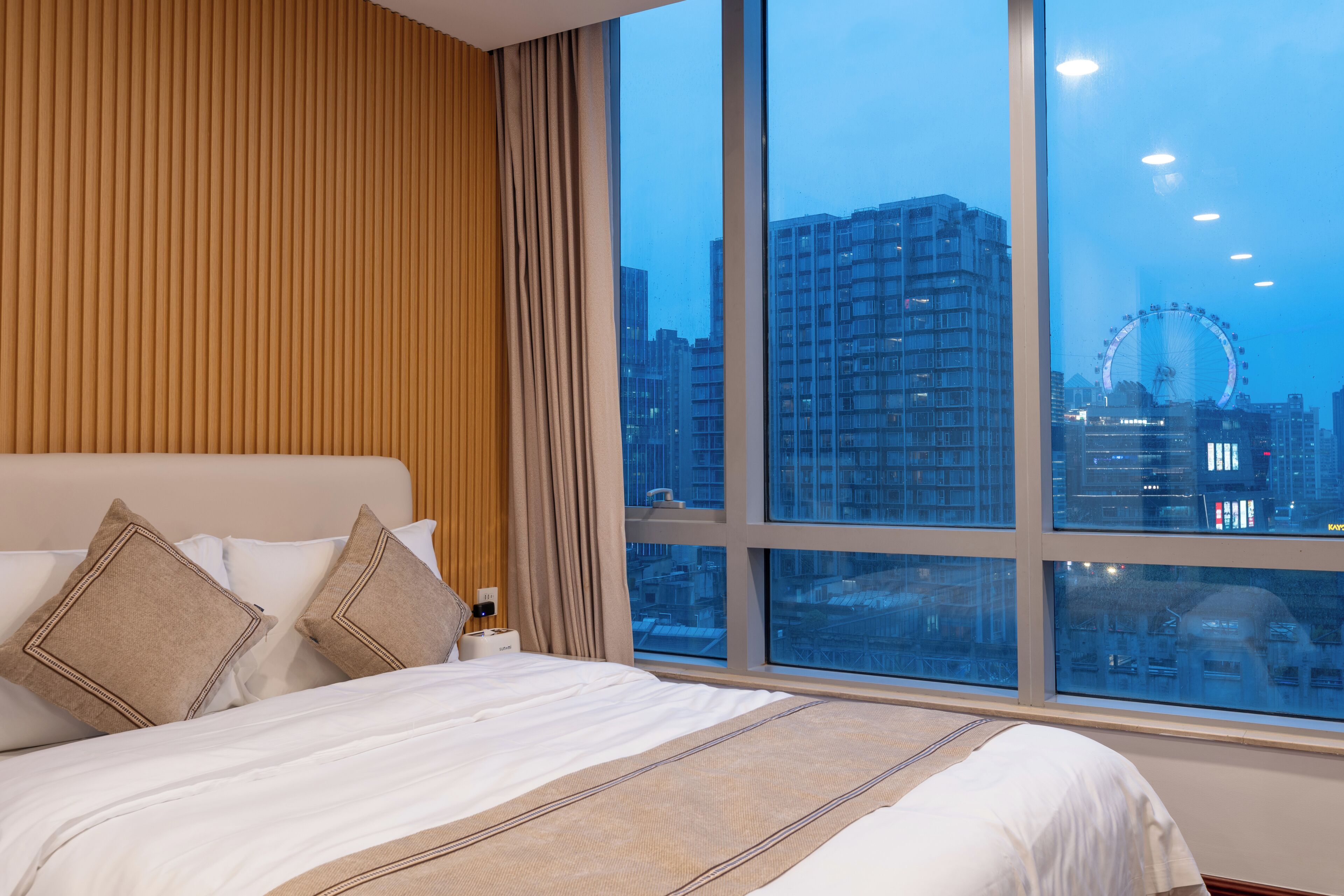 A hotel room with a large window, a bed with white bedding, and a view of a Ferris wheel.