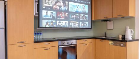 A kitchen with wooden cabinets, a built-in oven, a black countertop, and a large screen displaying various content.