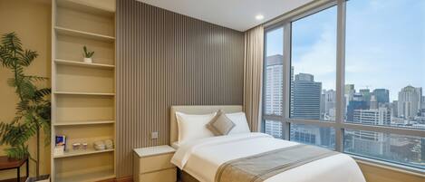 A modern hotel room with a large window, a bed, a bedside table, a shelf with a plant, and a view of the city skyline.