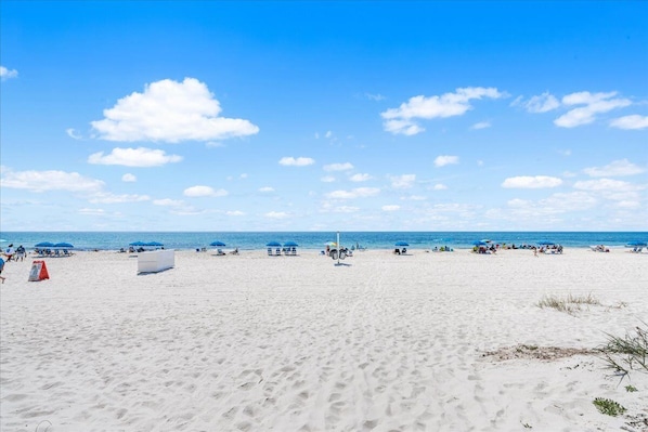 A sandy beach with umbrellas and a few people, a clear sky, and the ocean in the background. - Walkable Family Beach Base, Pet Friendly (Gulf Shores)
