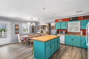 A kitchen with teal cabinets, a wooden island, and a dining area with a table and chairs. - Walkable Family Beach Base, Pet Friendly (Gulf Shores)