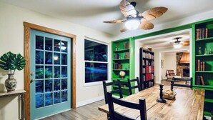 Ein Essbereich mit Holztisch und -stühlen, einem Deckenventilator und grünen Bücherregalen.