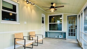 Ein Zimmer mit zwei Korbstühlen, einem Deckenventilator und großen Fenstern.