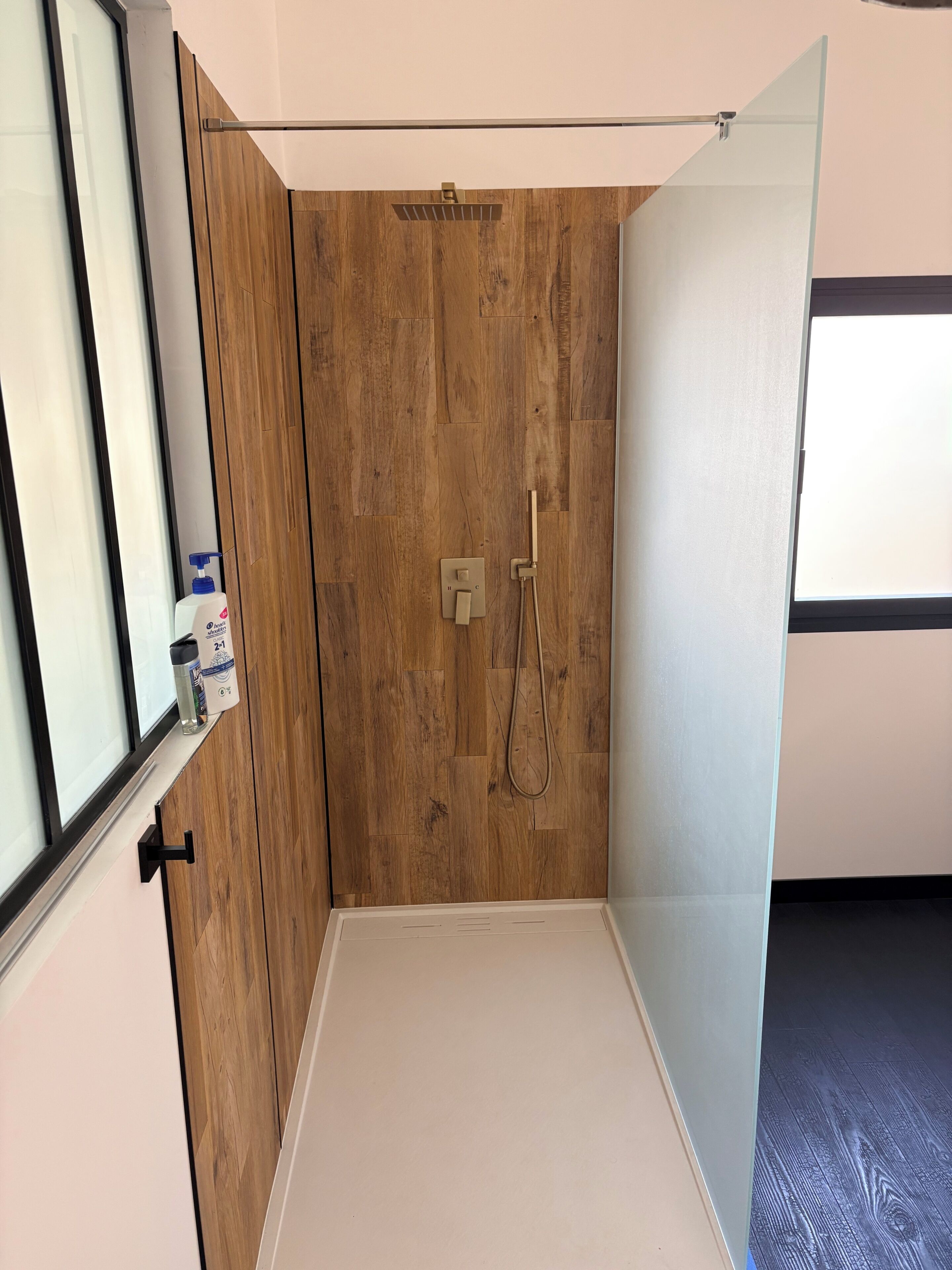 A shower room with a wooden wall, a glass door, and a white floor.