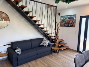 A modern living room with a dark sofa, a wooden staircase, and a painting of a vintage car.