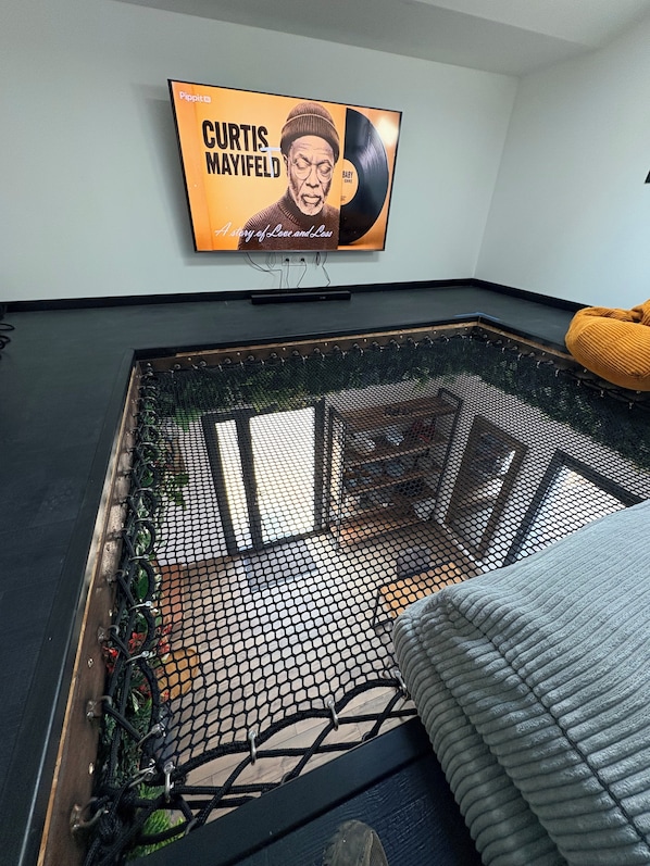 A room with a hammock, a television displaying a music album cover, and a window with a view.