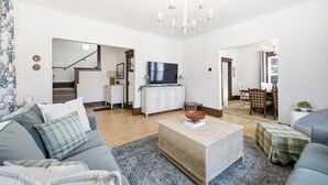 A spacious living room with a sofa, coffee table, and a television. There is a staircase leading to another level.