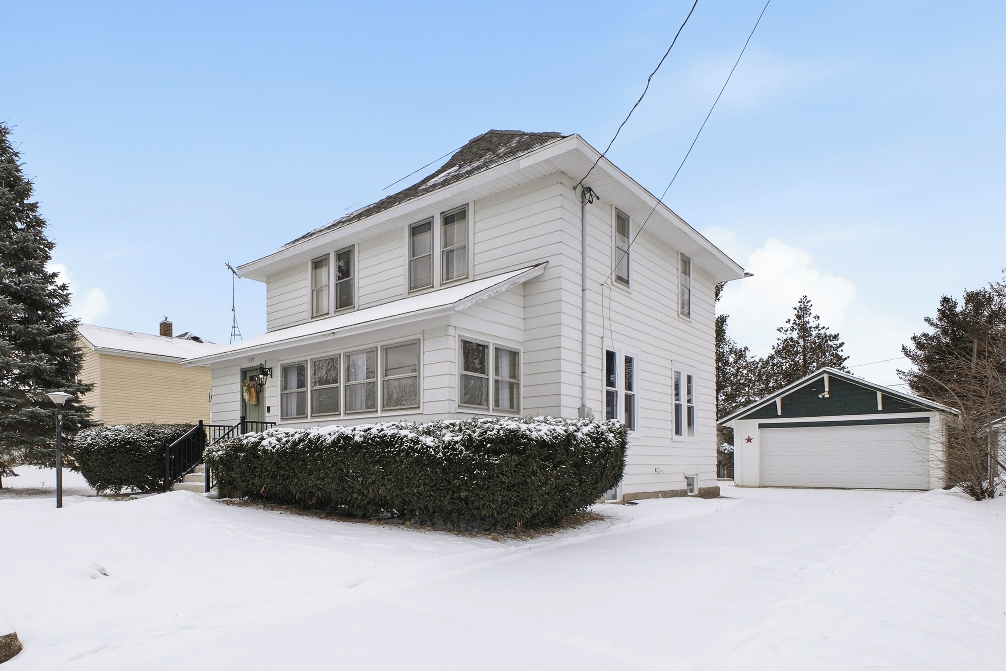 A two-story house with a garage, surrounded by snow-covered ground and trees.