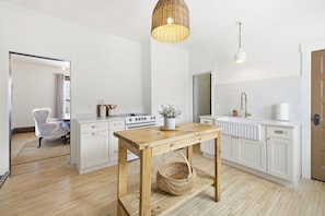 A modern kitchen with white cabinetry, a wooden table, a wicker basket, and a hanging light fixture. - Carefully curated and walkable to all Princeton has to offer. (Princeton)
