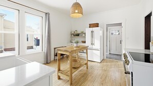 A kitchen with a wooden table, white cabinets, a refrigerator, and a hanging light fixture.