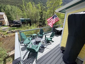 A deck with outdoor furniture, an American flag, and a view of a forested area.
