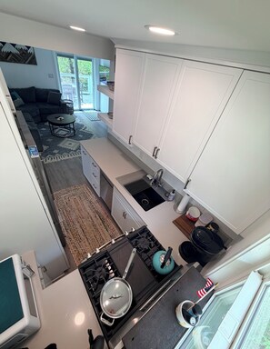 A modern kitchen with white cabinetry, a gas stove, and a sink. There is a dining area with a sofa and a coffee table.