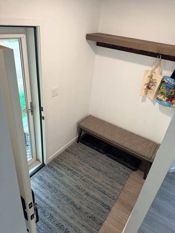 A room with a bench, a door leading outside, and a wall-mounted shelf with bags.