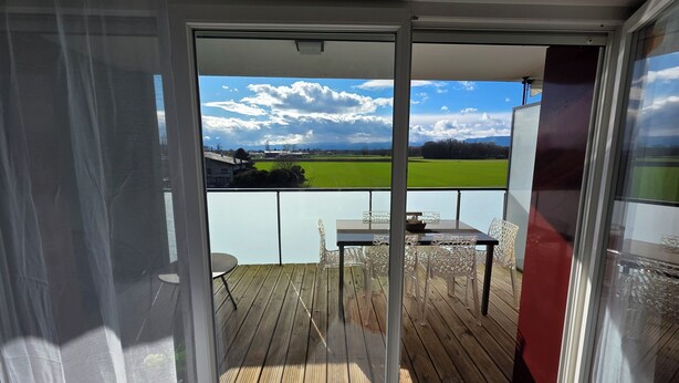 Een balkon met een tafel en stoelen, een uitzicht over een groen veld en een heldere lucht.