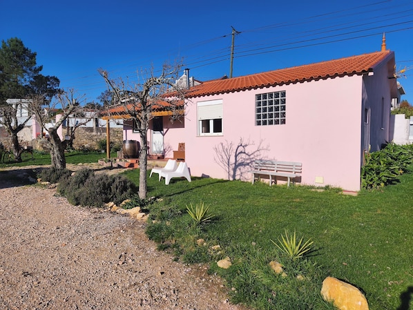 A pink house with a tiled roof, a small window, and a bench in the yard.