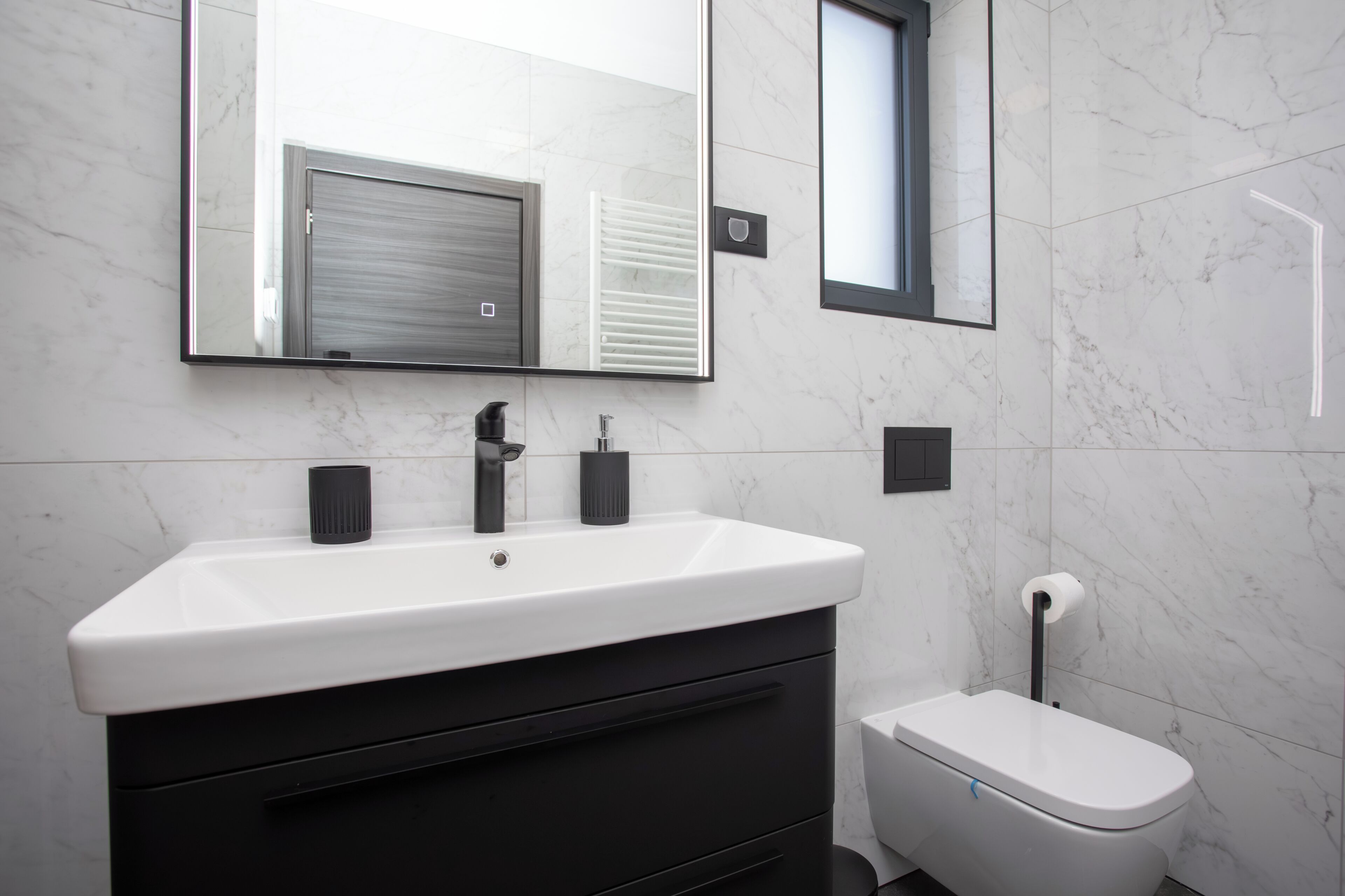 A modern bathroom with a white sink, black faucet, and a toilet.