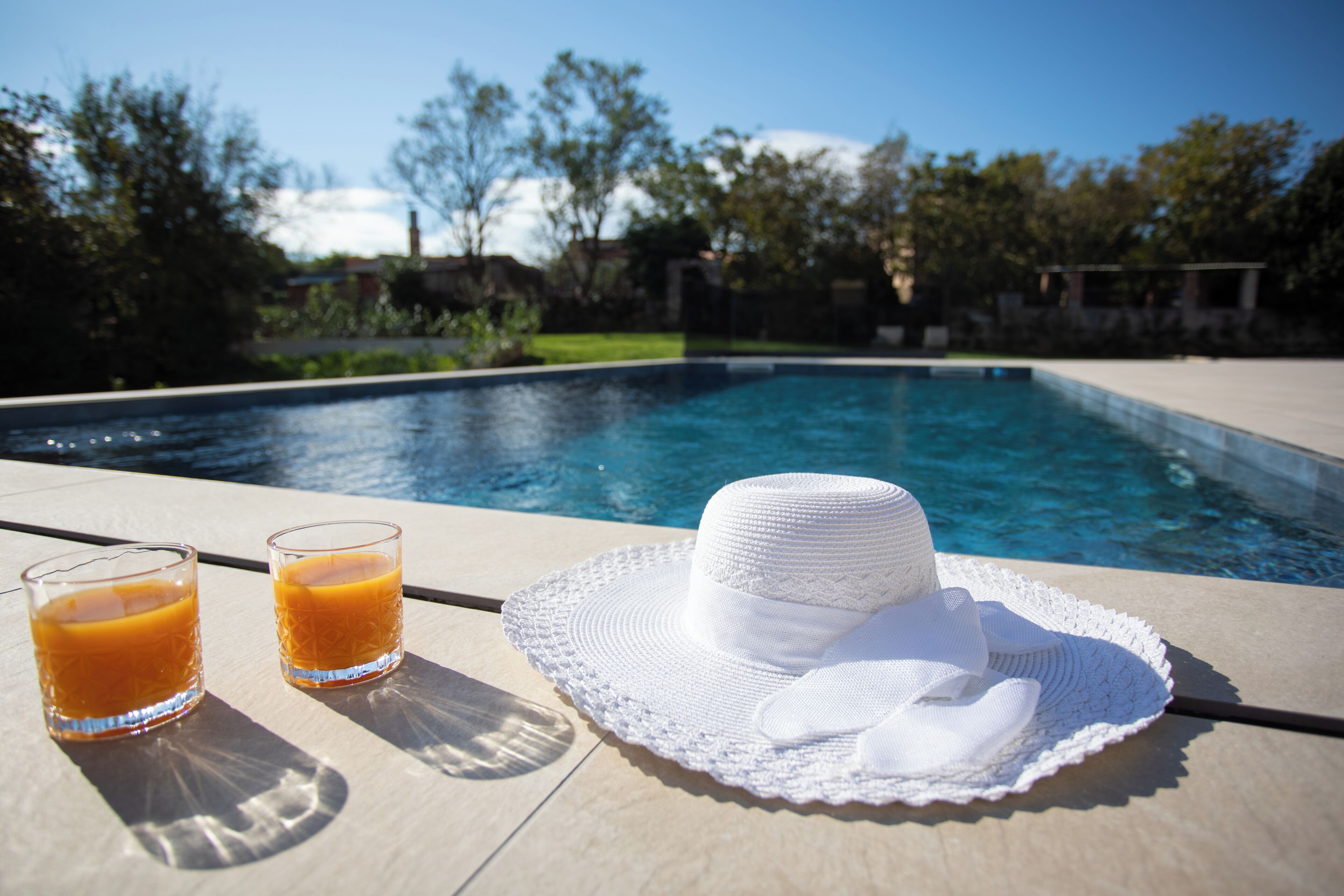 Ein Poolbereich mit einem weißen Hut und zwei Gläsern Orangensaft auf einem Tisch.