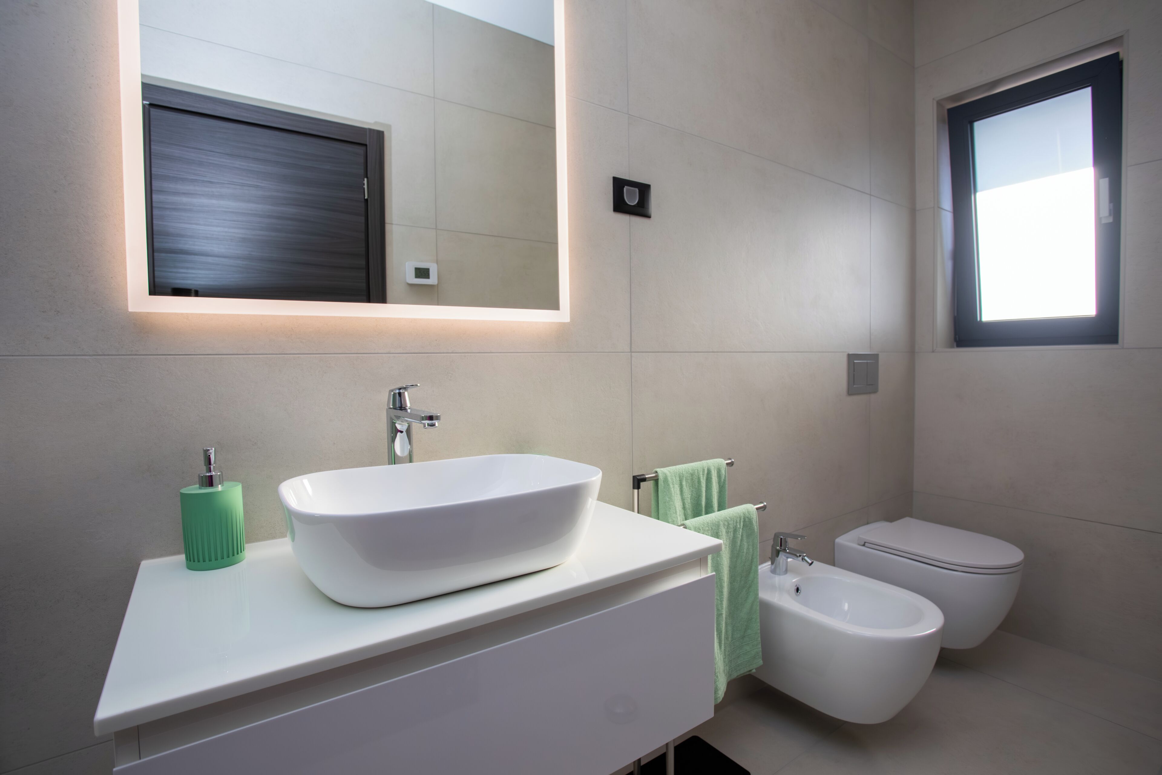 A modern bathroom with a white sink, green soap dispenser, and a bidet.