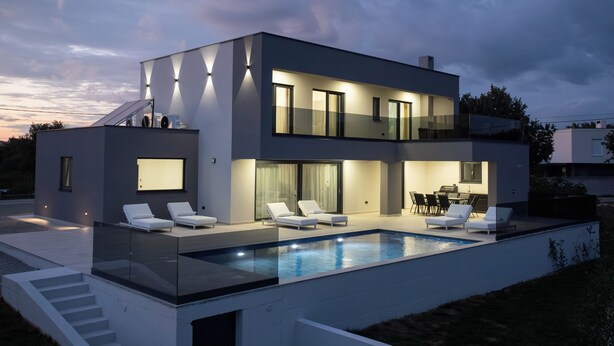 Una casa moderna de dos pisos con piscina, sillas de descanso y comedor.